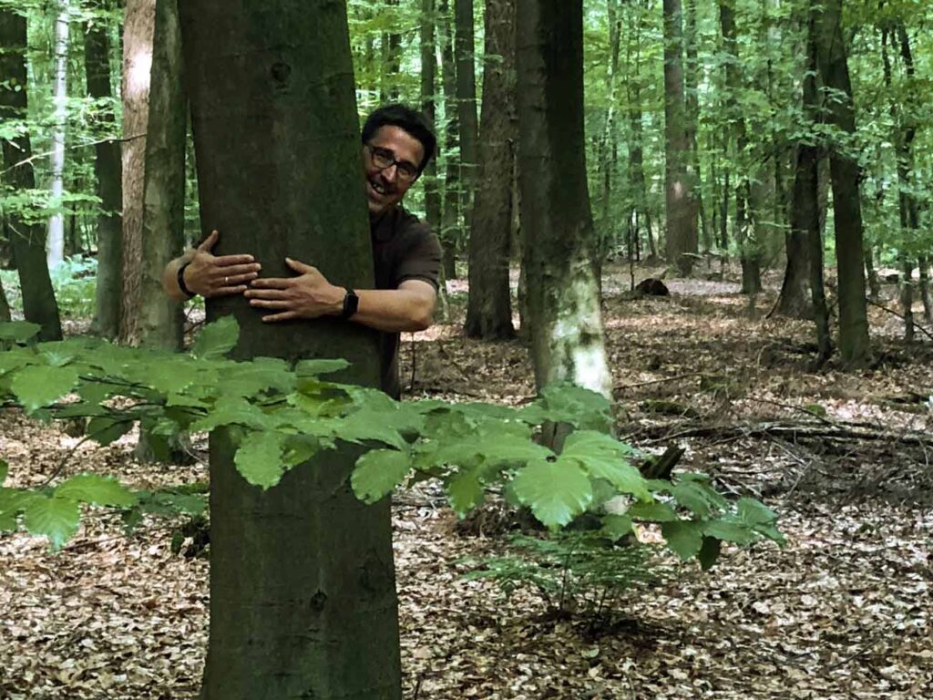 René Schneider umarmt einen Baum im Wald.